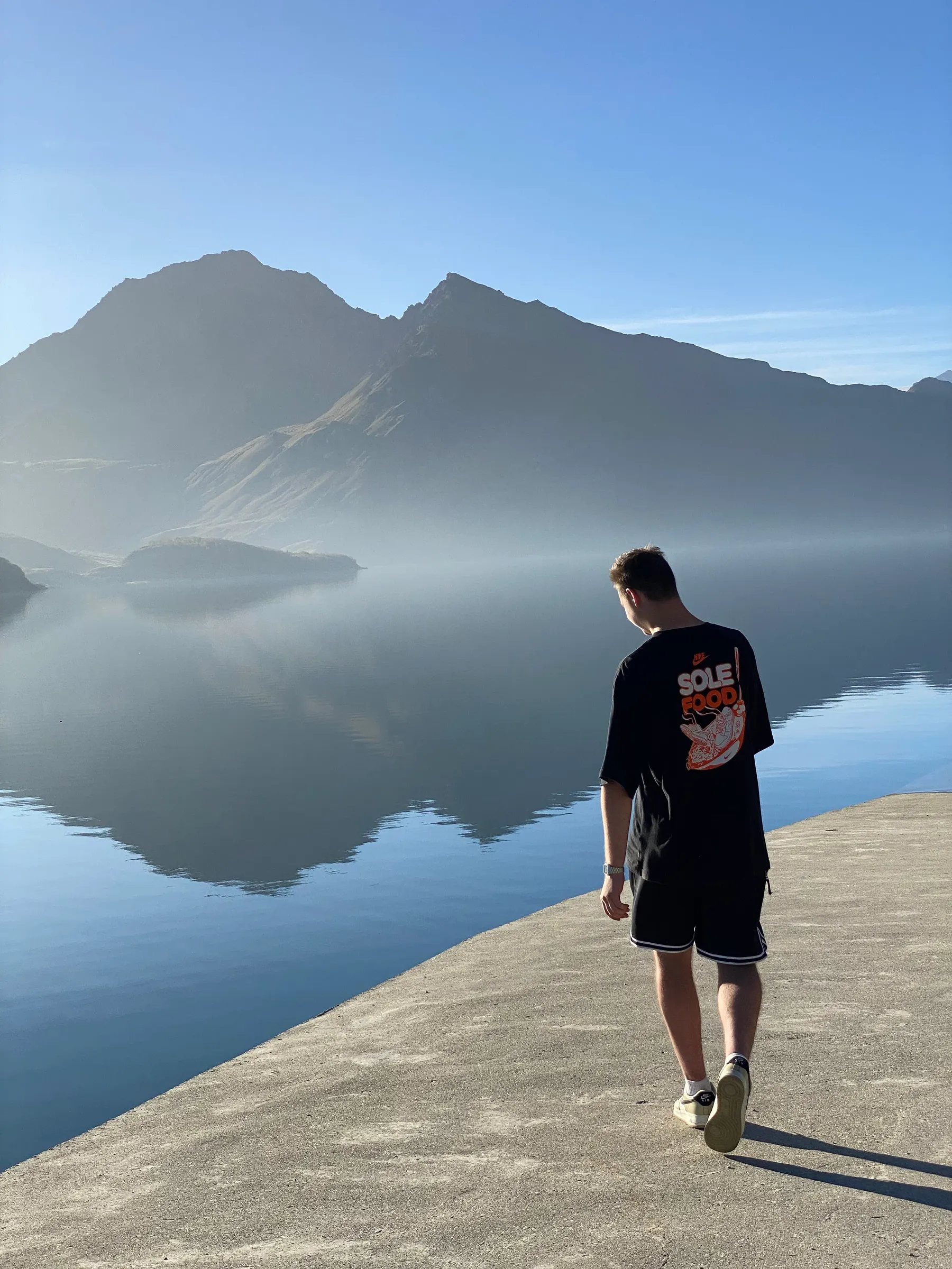 A young person walking by a lake and looking into the distance